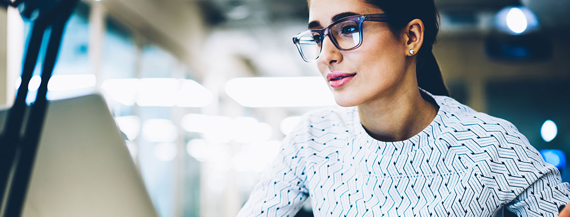 A woman wearing glasses and looking at a computer