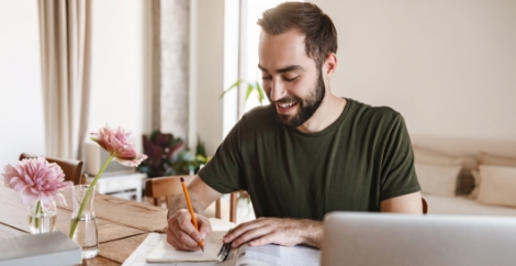 Man in black t-shirt writing notes at his desk