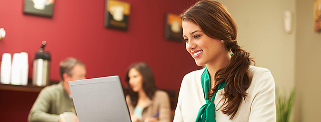 Woman in a cafe reading the CFA Program fundamentals free eBook on her laptop