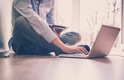 Man sitting on the floor attending an online class on a laptop.