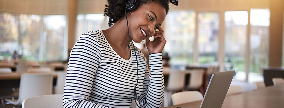 Woman wearing headphones sitting at large conference table working on a laptop image