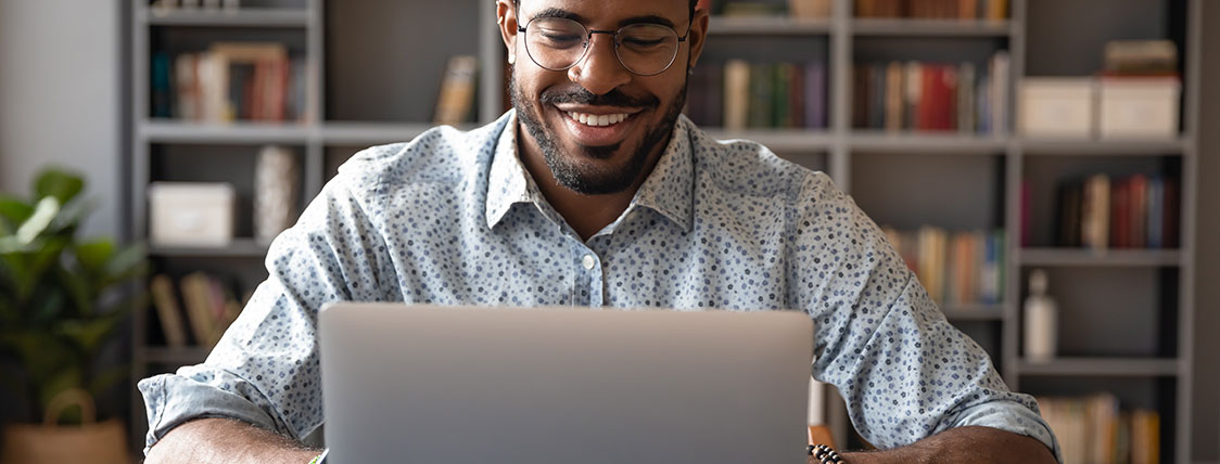 Man working on a laptop with large bookcase behind him image