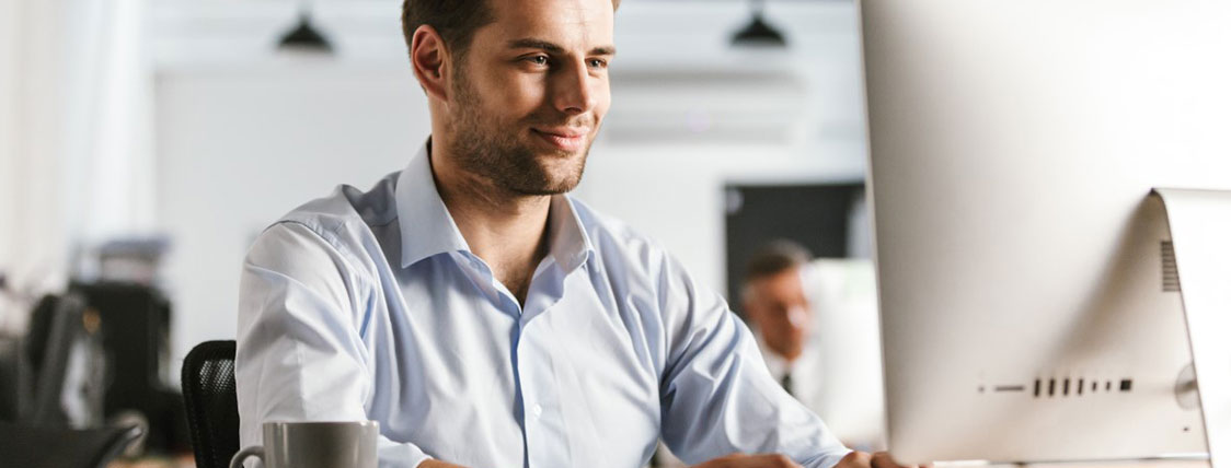 Man in an office sitting at desk in front of computer monitor image