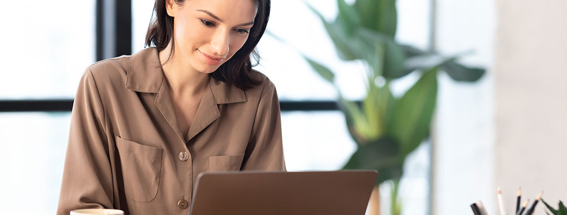 Woman working at a laptop with a window and a plant behind her image