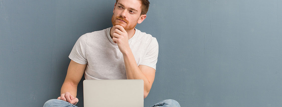 Man with quizzical expression sitting with laptop in his lap and hand on his chin image