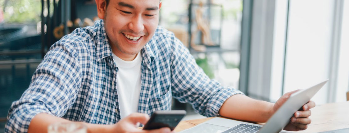 Man sitting at a table in front of a laptop reading a message on his phone image