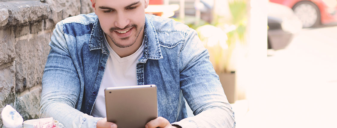 Man sitting outside next to stone wall working on a tablet device image