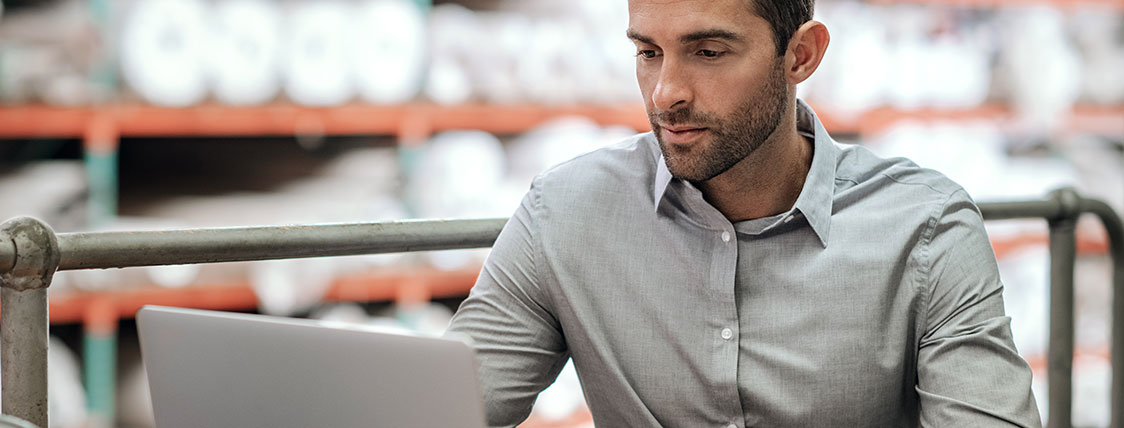 Man seated in a warehouse working on a laptop image