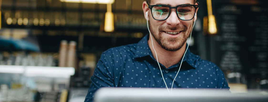 Man wearing earbuds working on a laptop in a coffee shop image