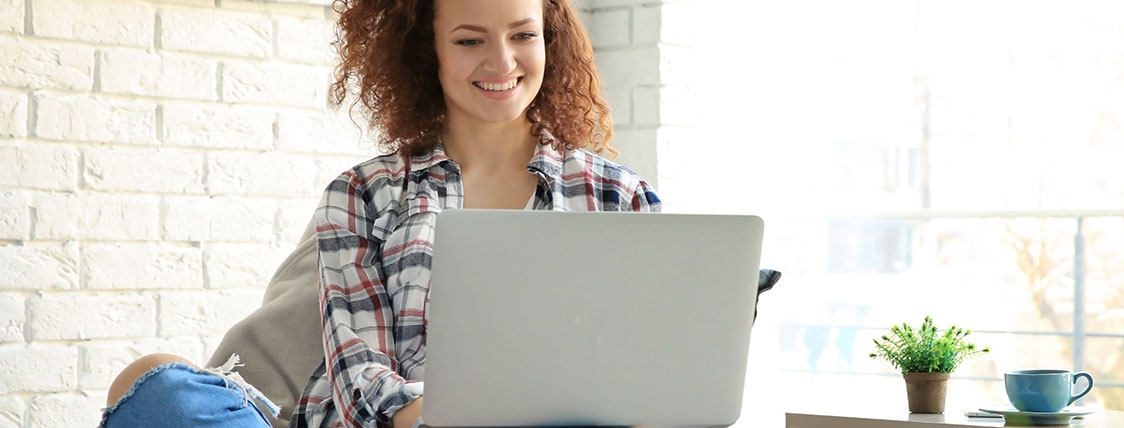 Woman sitting in front of a white brick wall working on a laptop image
