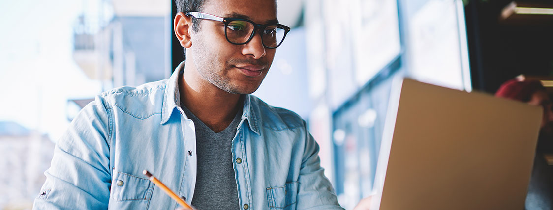 Man holding a pencil looking at an open laptop image