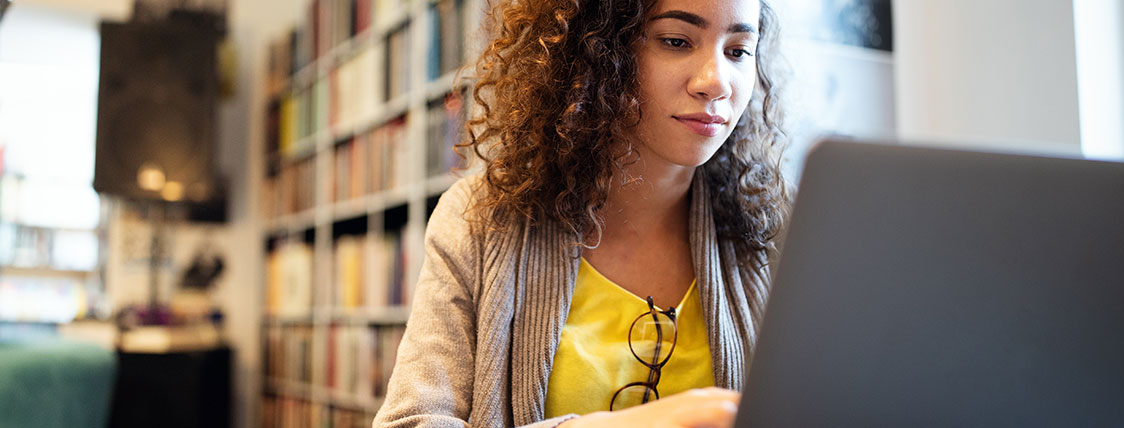 Woman working on a laptop with a bookcase behind her image