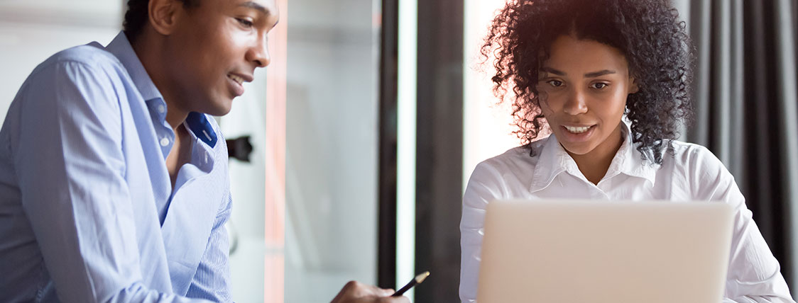 Two colleagues sitting side by side looking at a laptop screen together image