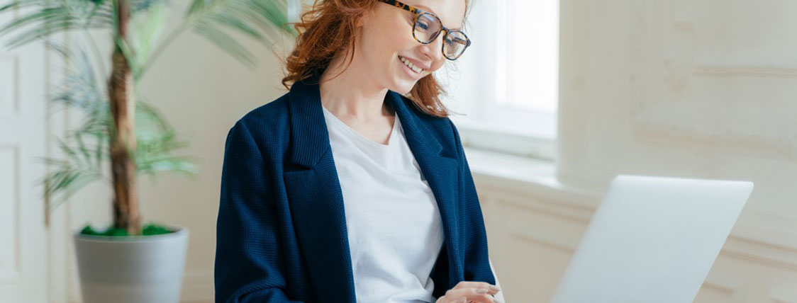 Woman working on a laptop with a large plant behind her image