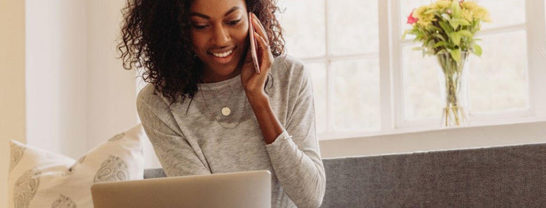 Woman sitting on a sofa working on a laptop and talking on a cell phone image