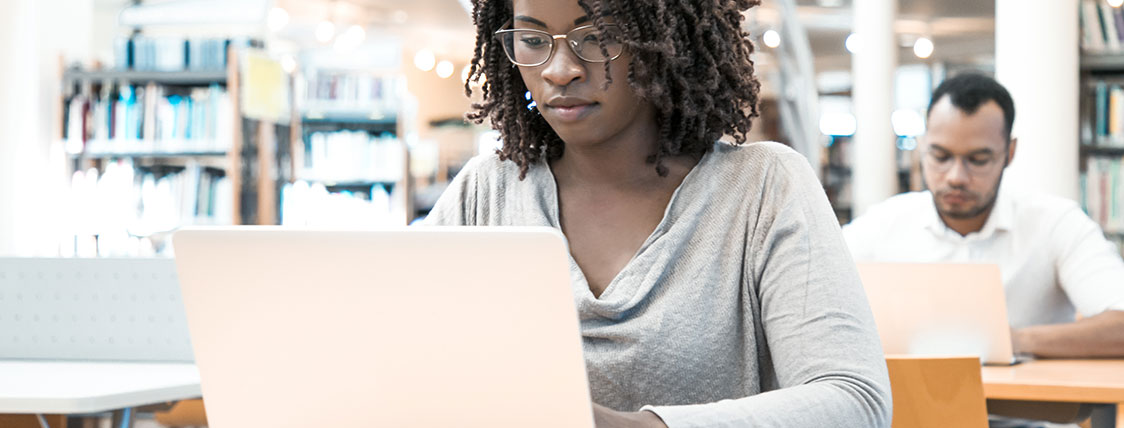 Woman sitting at a table working on a laptop in a library image