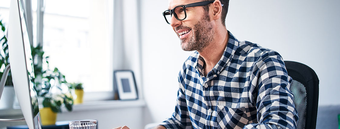 Man in plaid shirt working on a computer at a desk with a monitor image