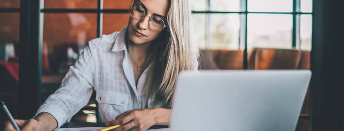 Woman sitting at table with laptop taking notes in a coffee shop image