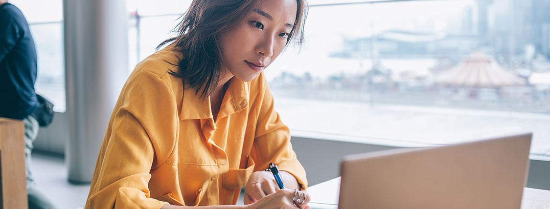 Woman sitting at table in front of window working on a laptop image