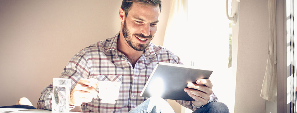 Man sitting holding a coffee cup and a tablet device image