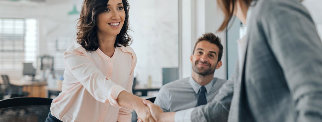 Two people shaking hands in an office with another colleague looking on image