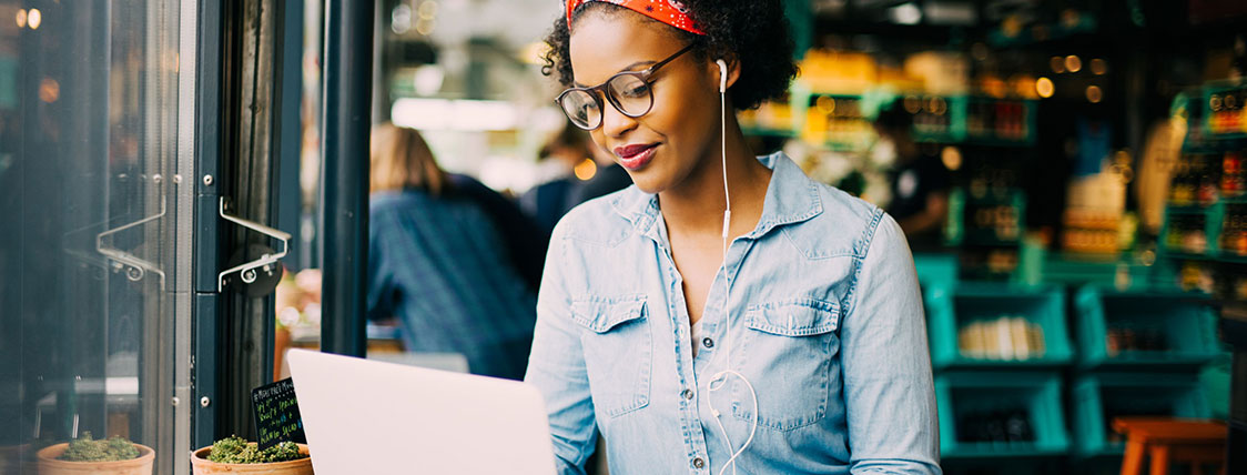 Woman wearing earbuds working on a laptop in a coffee shop image
