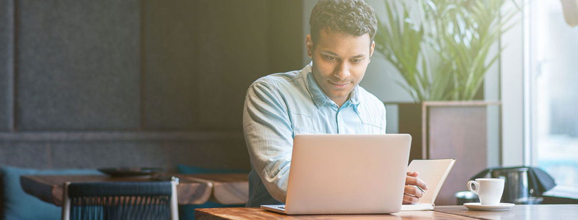 Man sitting at a table in a coffee shop working on a laptop image