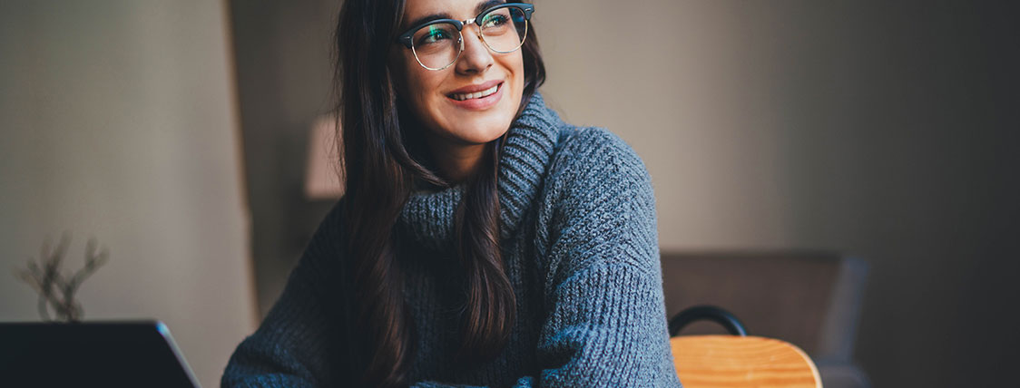 Woman in blue sweater sitting at a table with an open laptop image